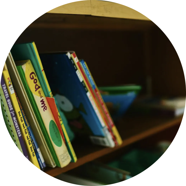 A row of children’s books standing upright on a wooden bookshelf, with some book titles partially visible.